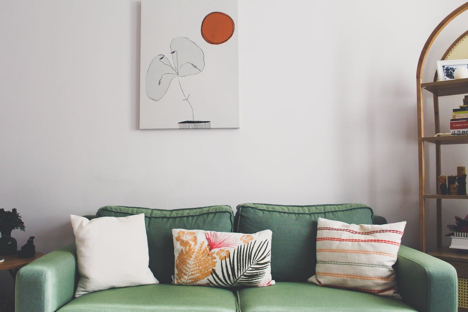 A minimalist abstract canvas with an orange sun motif hanging above a green velvet sofa with patterned cushions.