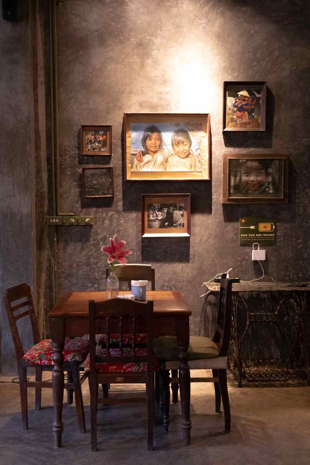 Cluster of framed portrait photographs grouped on a dark concrete wall above a wooden table