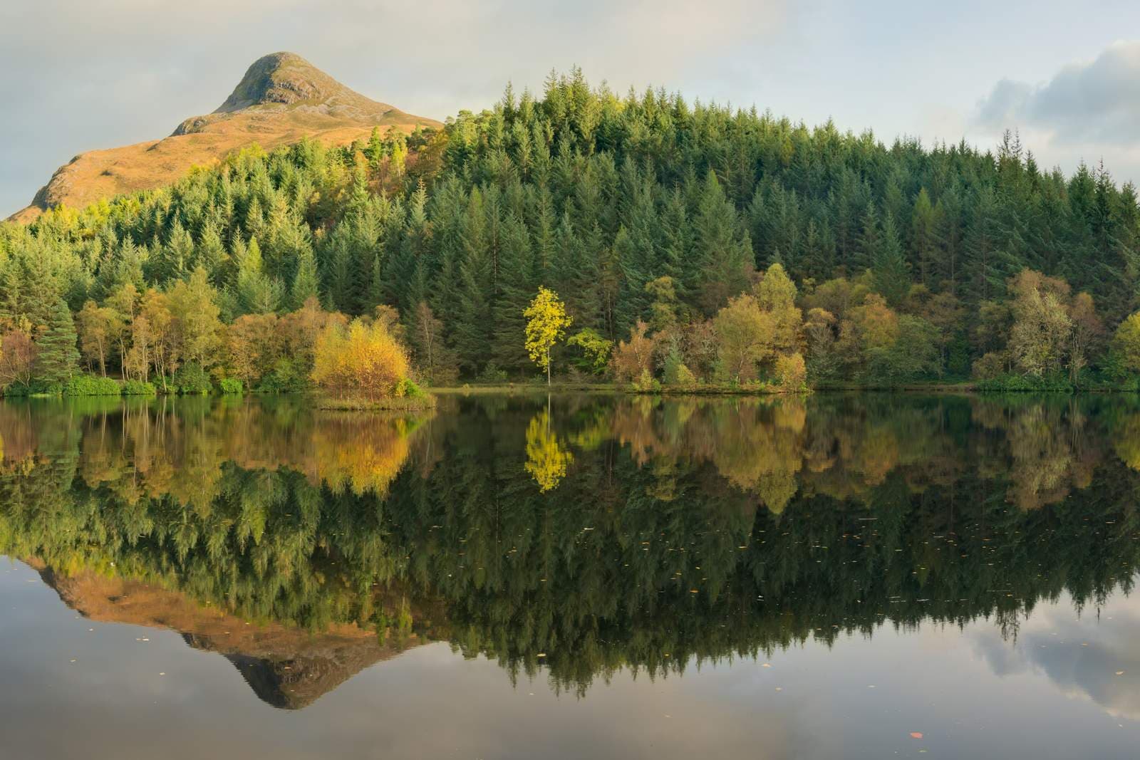 A forested hill and peak reflected perfectly in the still water of Glencoe Lochan, Scotland