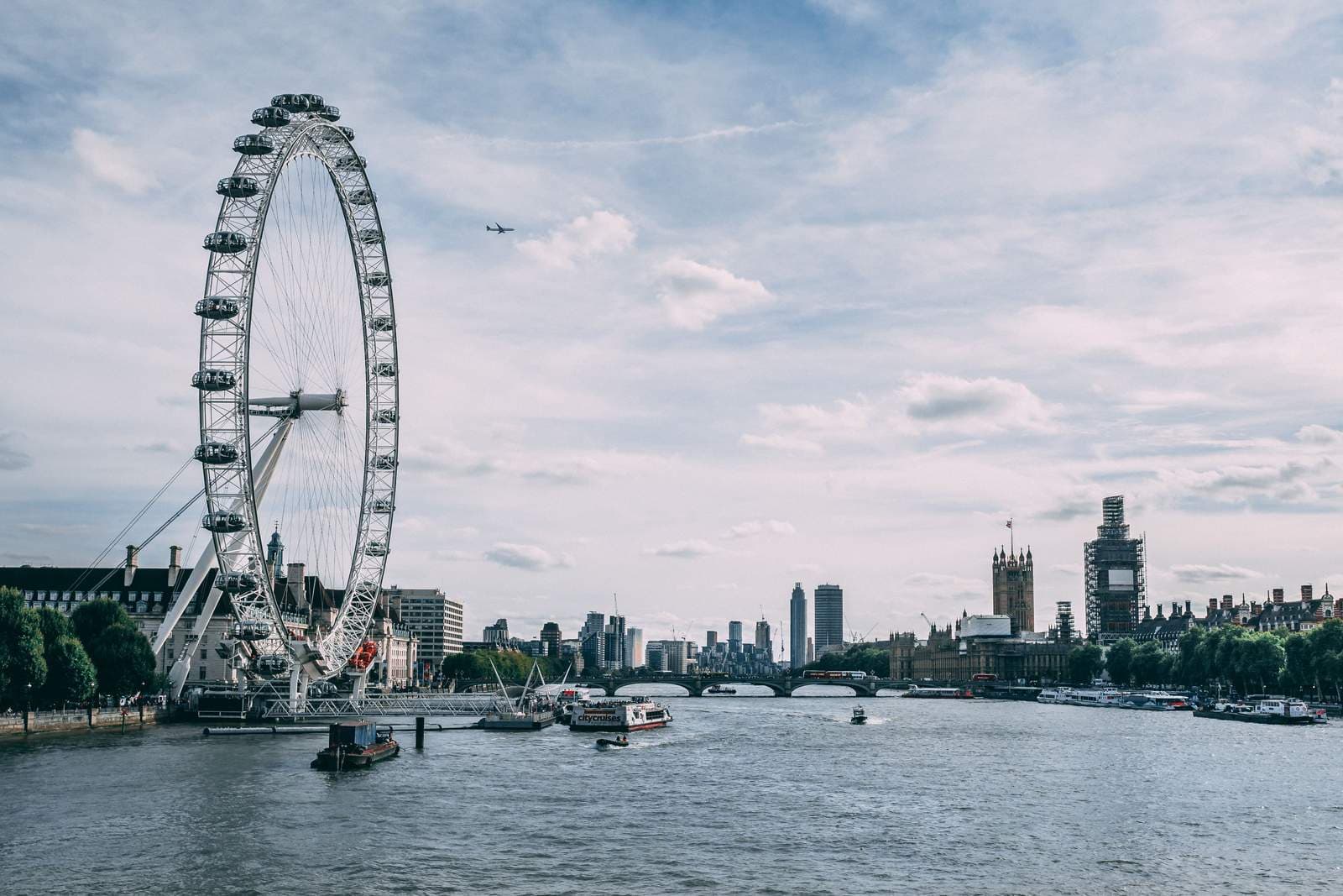 The London Eye and the Westminster skyline across the River Thames under a partly cloudy sky