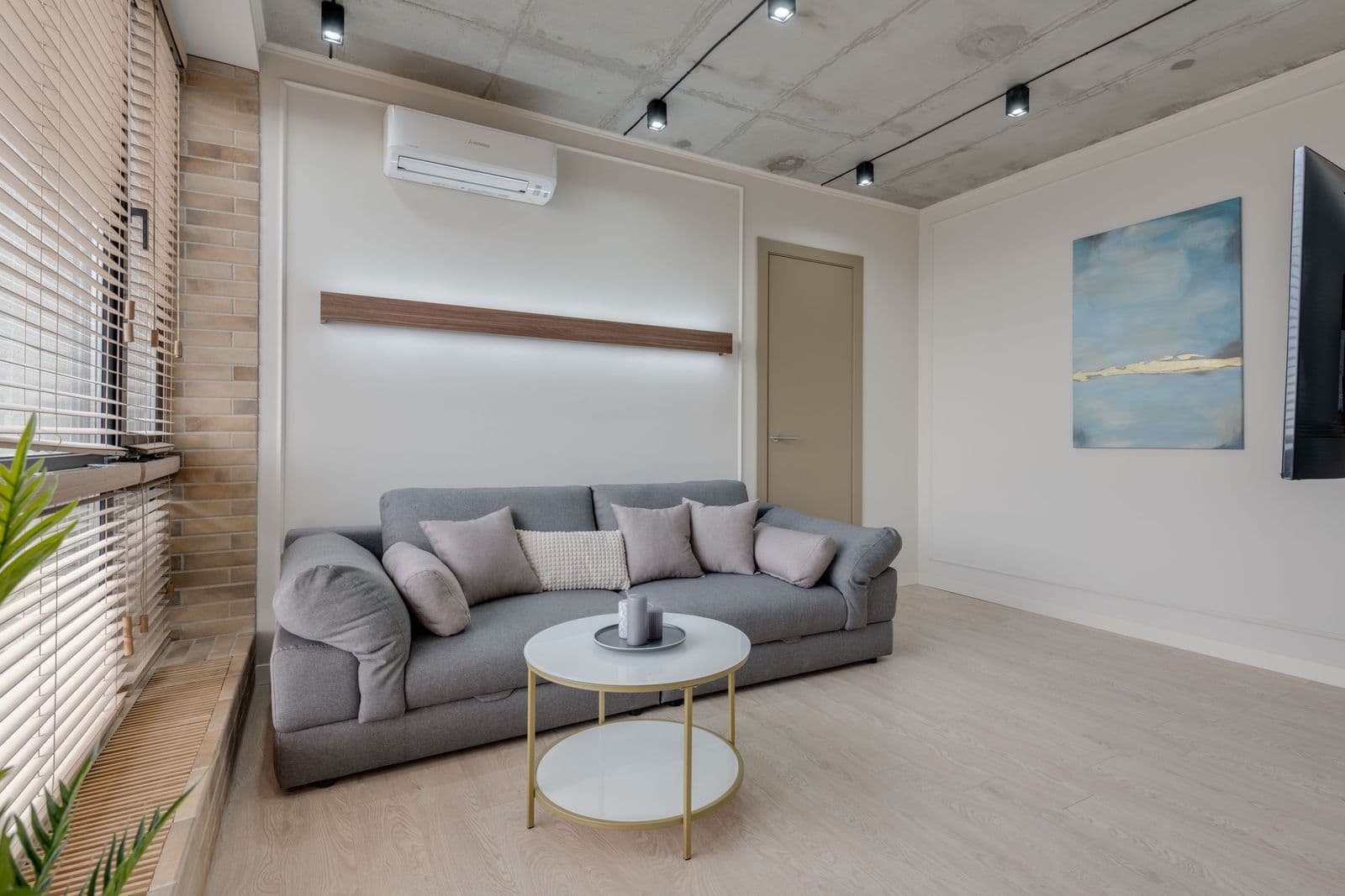 A spare living room with a gray sofa, bare walls and a single soft blue abstract canvas as the only artwork