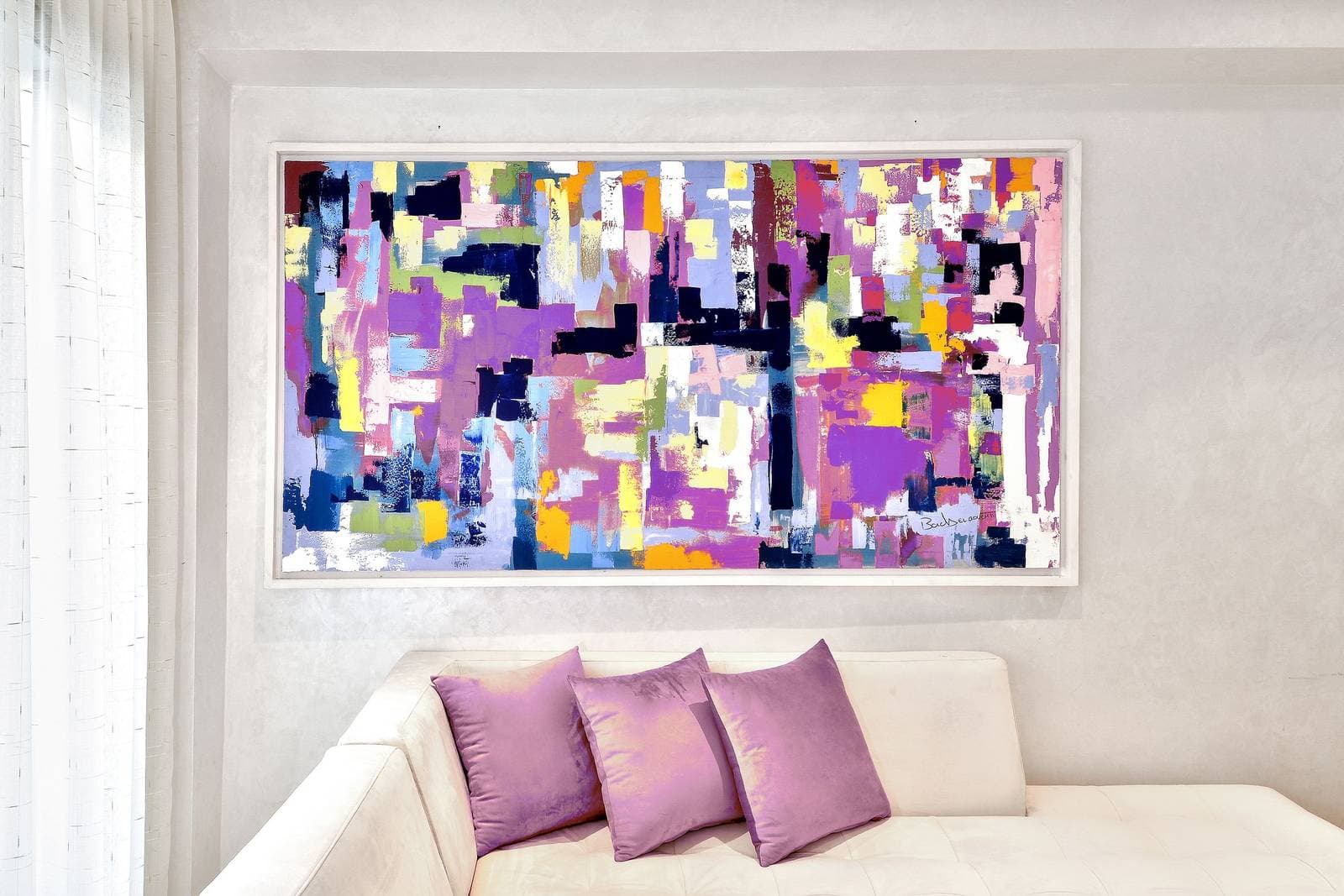 A large colorful abstract canvas in purple, pink and yellow hanging above a white sofa with lilac cushions