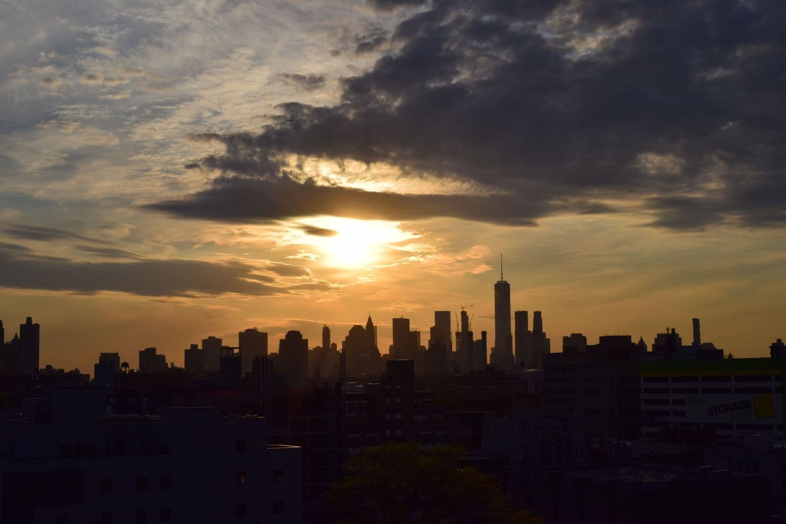 The Manhattan skyline silhouetted against a golden sunset, with One World Trade Center rising over the rooftops.