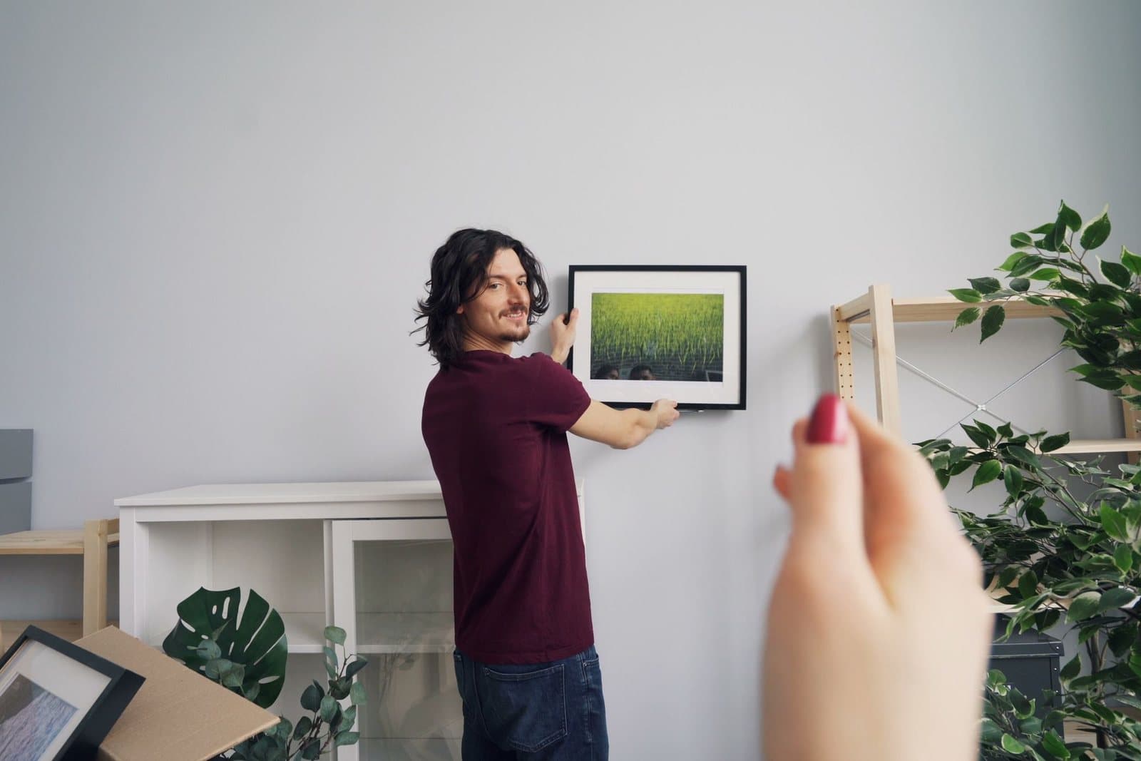 A man hanging a framed landscape photograph on a white wall in a bright new home.