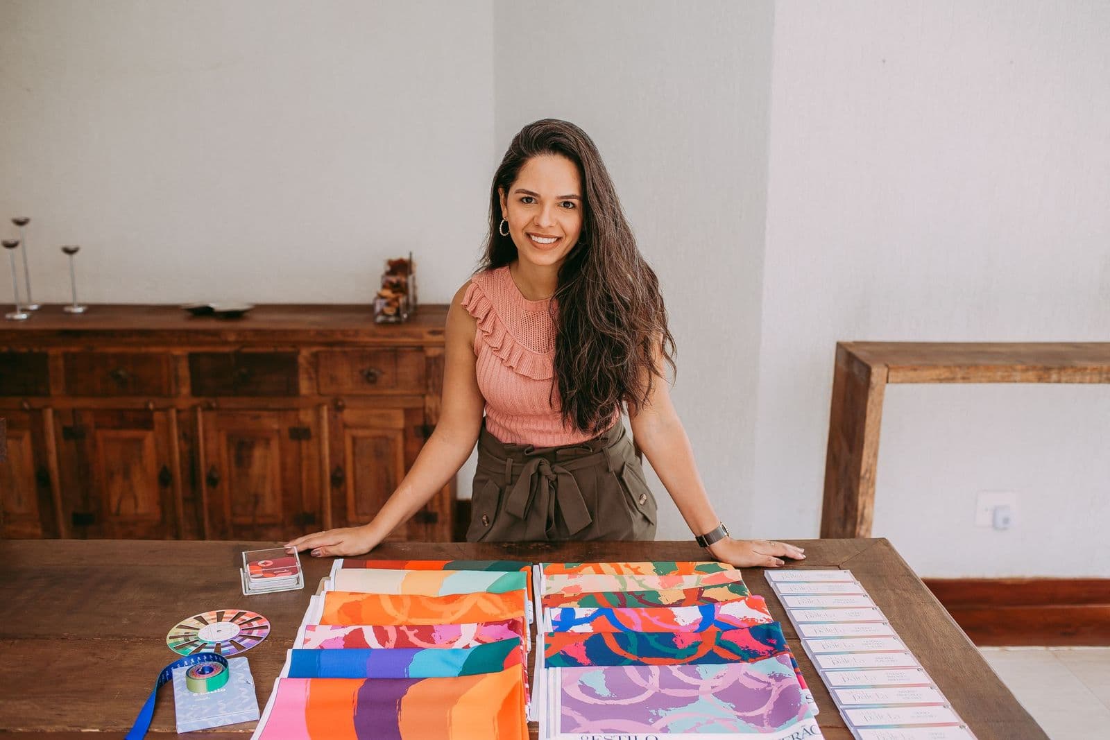 An interior designer standing at a studio table covered with colorful fabric and art samples.