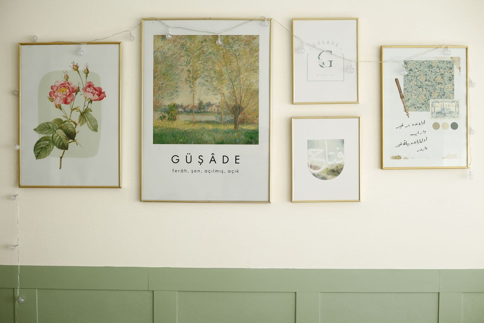 A gallery wall of framed prints in slim gold frames — a pink botanical rose, an impressionist landscape and typographic art — above sage-green wainscoting