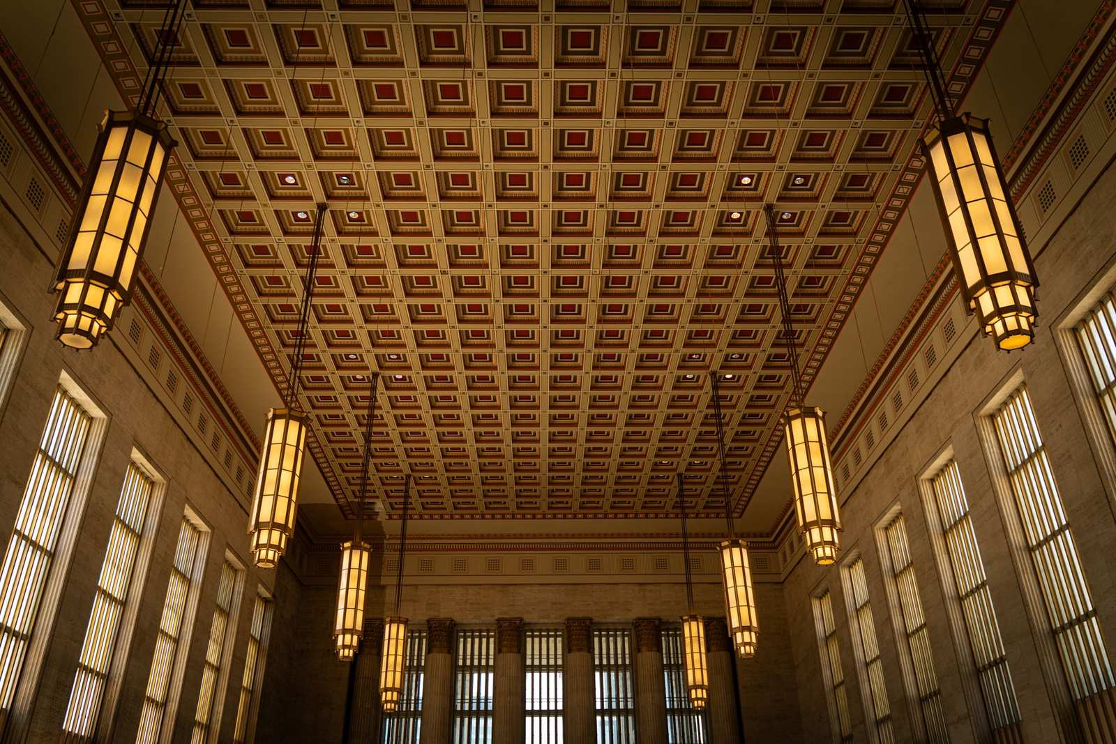 An Art Deco hall interior in Philadelphia with a geometric coffered ceiling, tall fluted windows and glowing rectangular lantern pendants