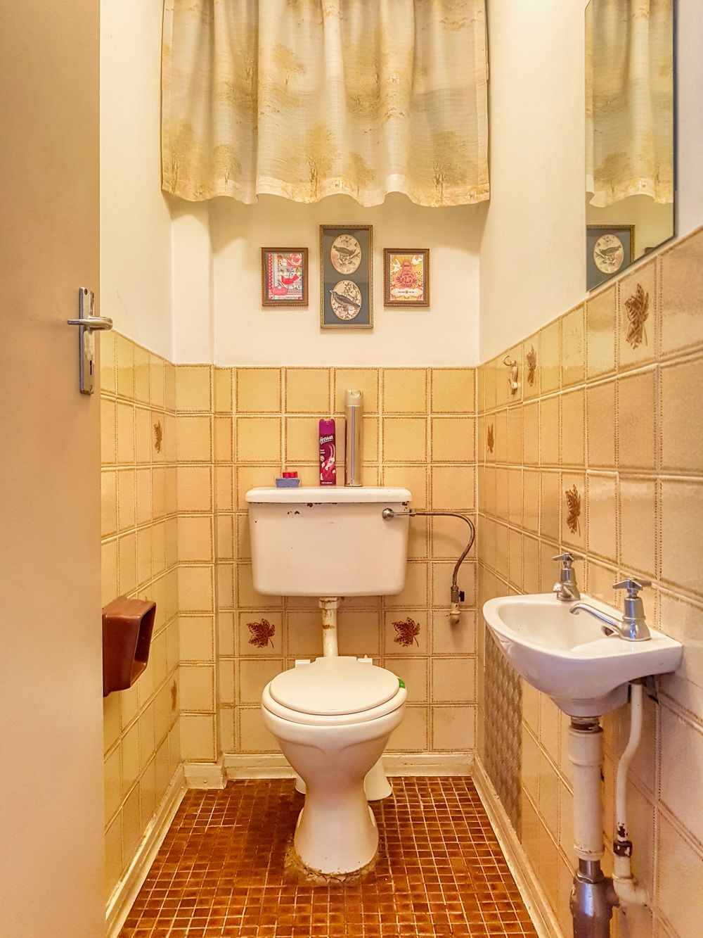 Small tiled bathroom with three framed pictures hanging on the wall above the toilet