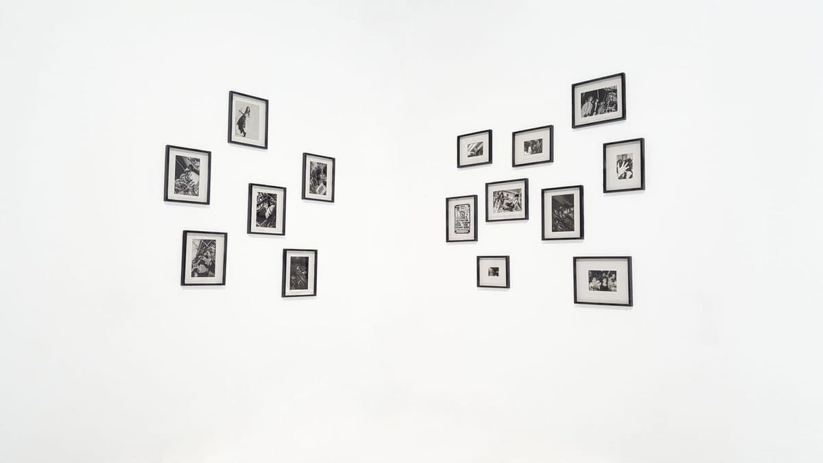 Two clusters of small black-and-white framed photographs arranged on a white gallery wall