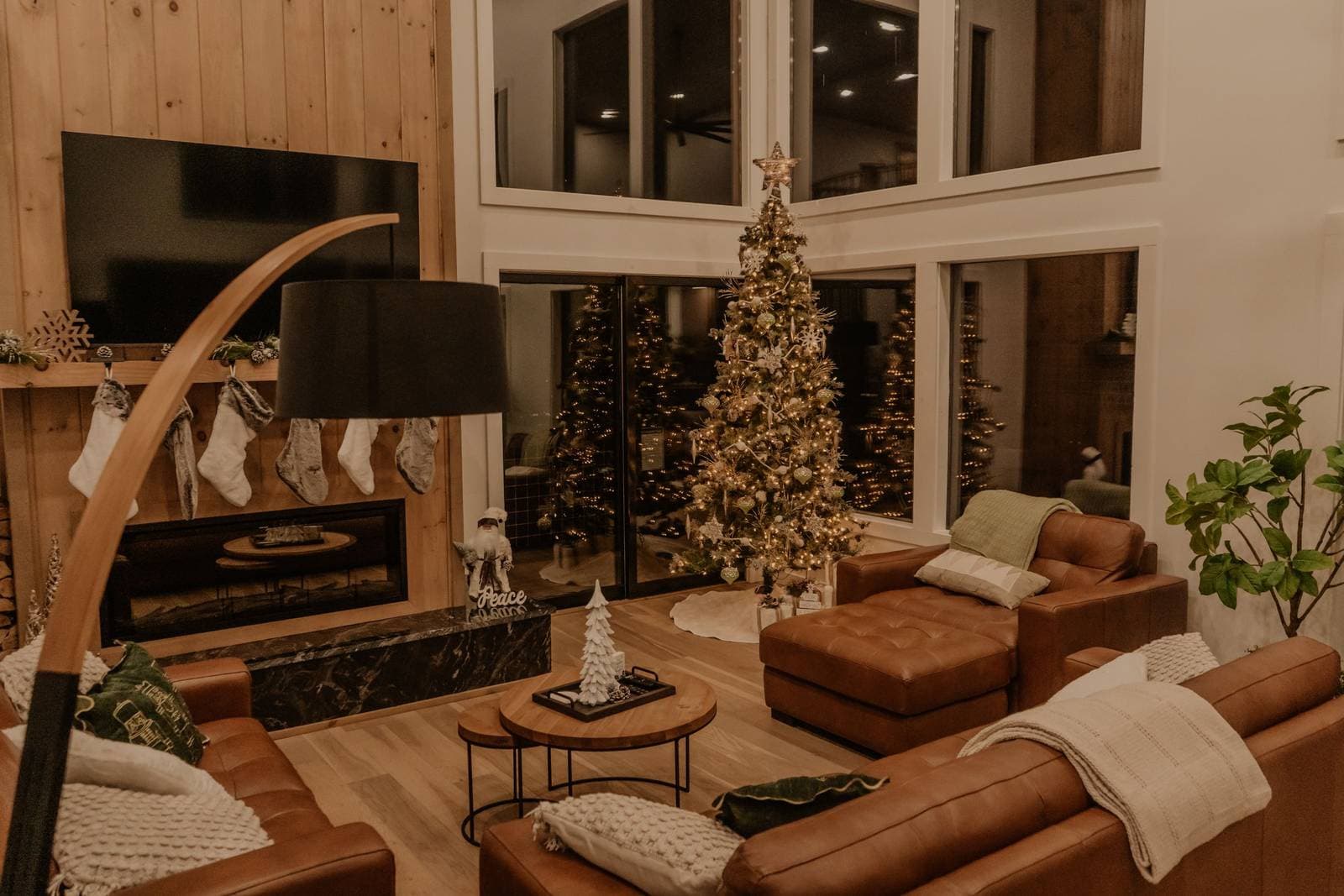 A warm living room decorated for Christmas with a lit tree, stockings hung over the fireplace and leather sofas.