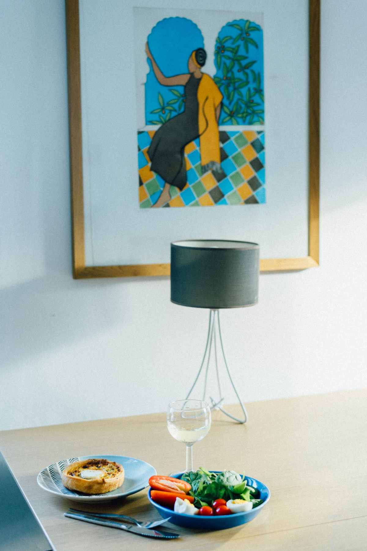 Framed colorful artwork hanging above a dining table set with a salad bowl and a tart