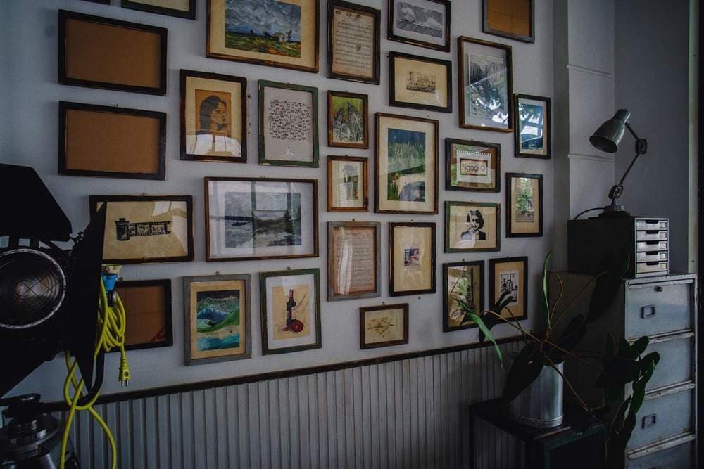 Dense eclectic gallery wall of mixed framed paintings, prints and sheet music in a studio room