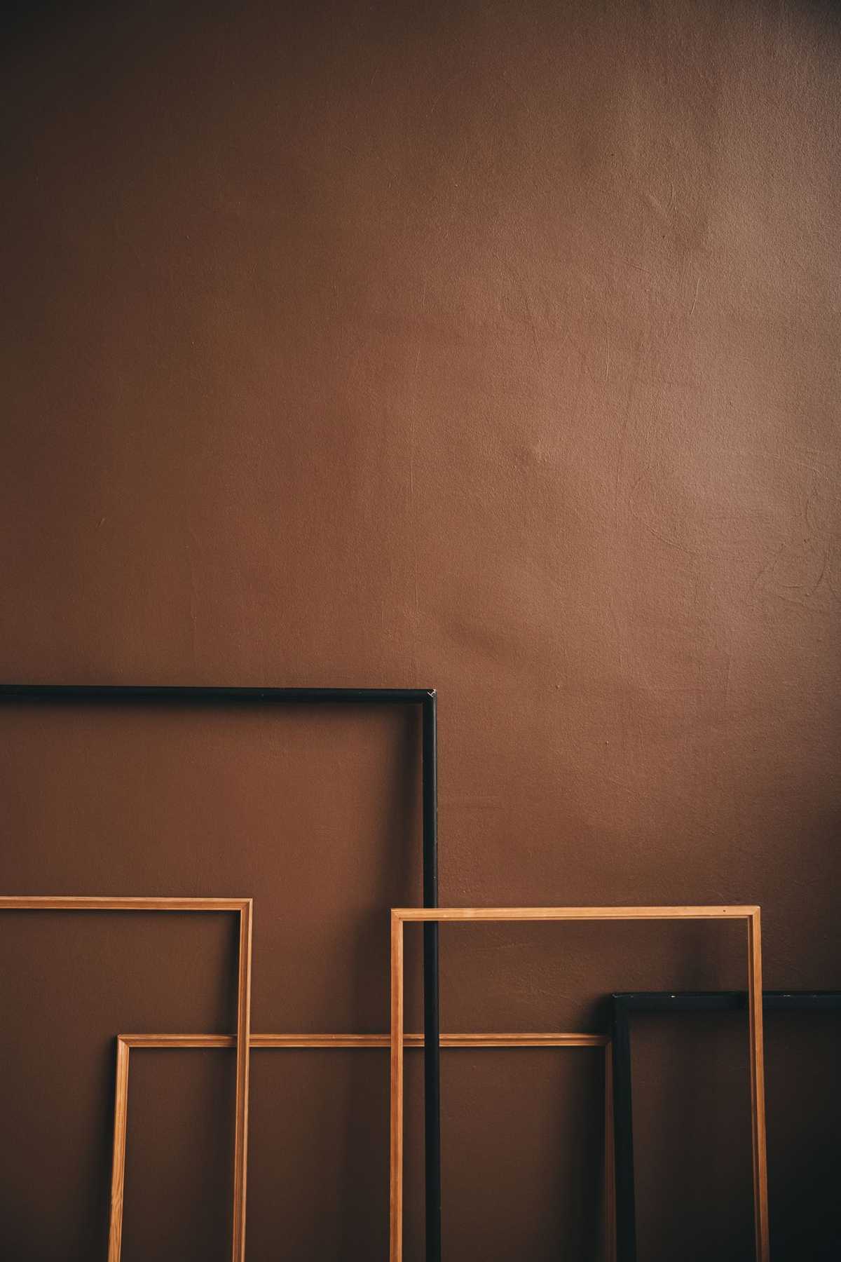 Empty wooden and black picture frames leaning against a brown wall, none of them hung