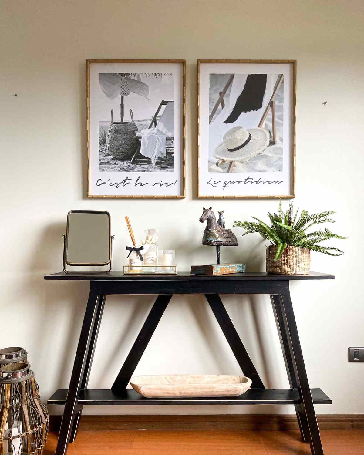 Two framed prints above a black console table styled with a small mirror, candle tray and potted fern
