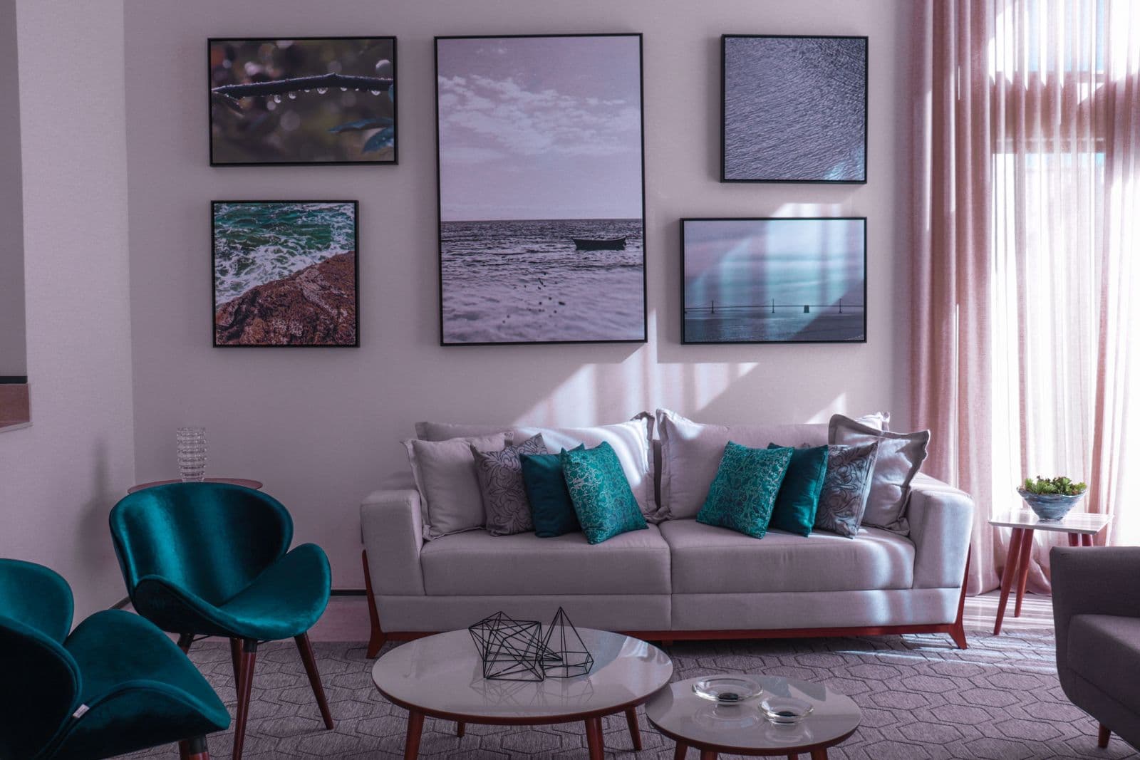 A living room gallery wall of five framed photographic prints in slim black frames arranged above a light grey sofa with teal cushions.