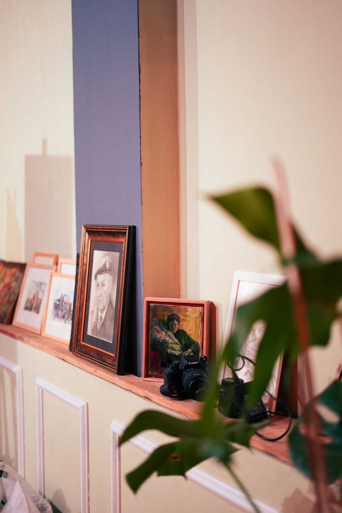 Framed photographs leaning in a row along a narrow picture ledge on a wall