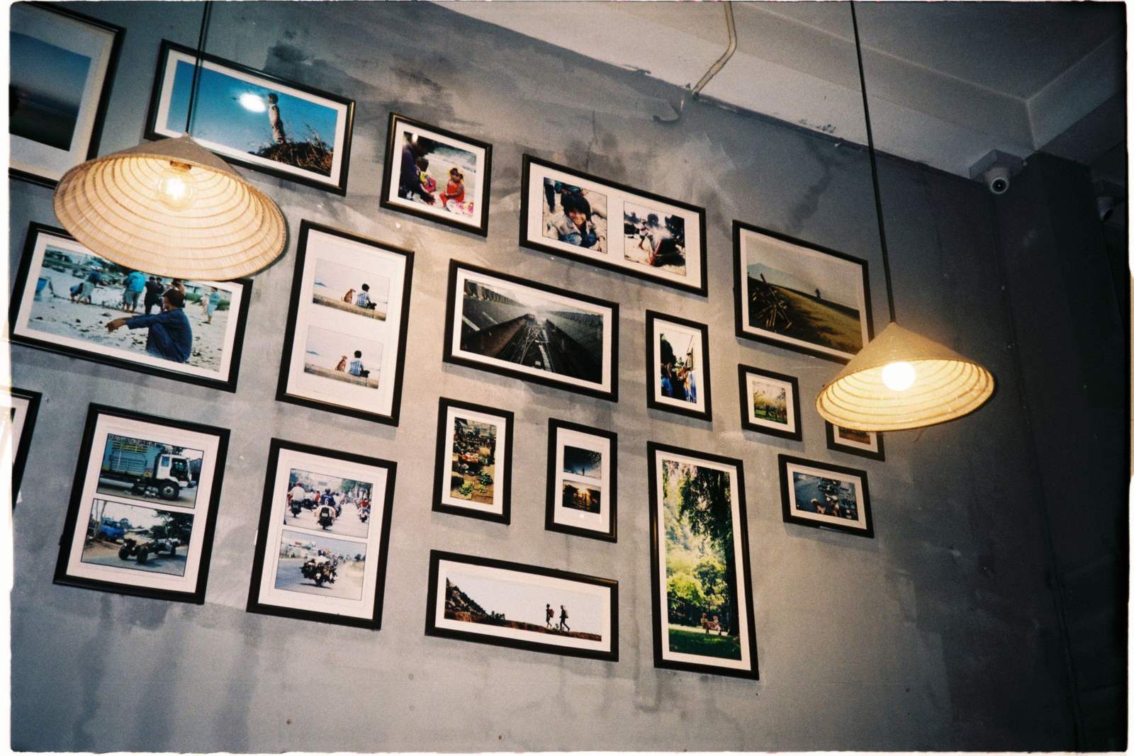 A salon-style gallery wall of black-framed photographs in mixed sizes arranged across a gray wall beneath two pendant lamps.