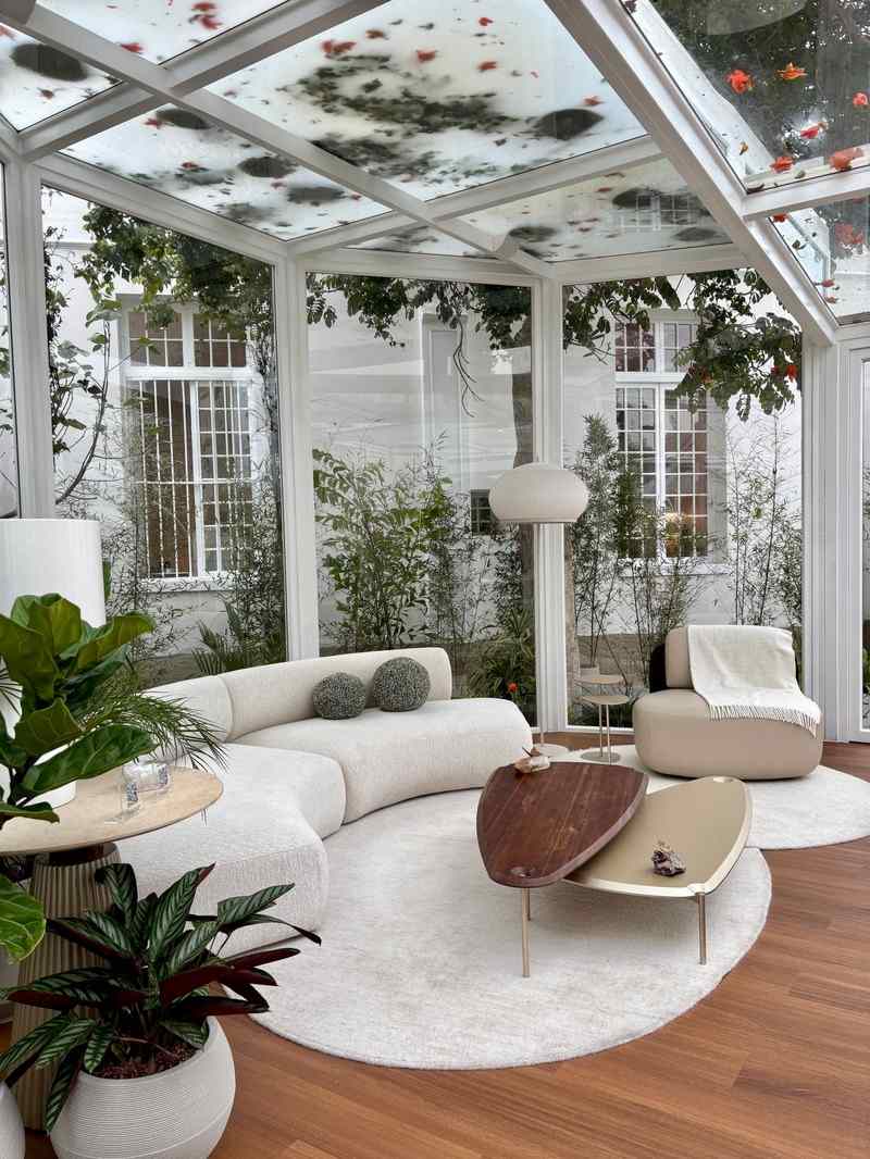 Bright glass sunroom with a curved sofa, armchair and indoor plants looking out to a garden