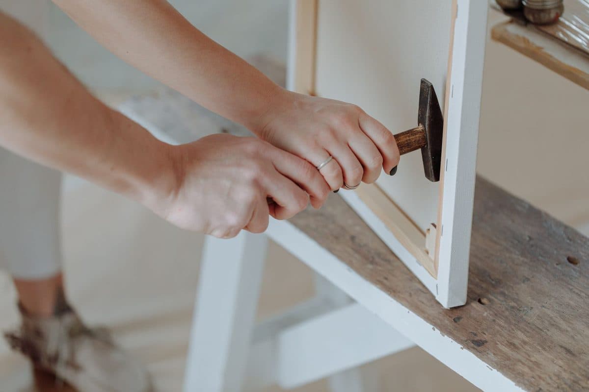 Hands using a hammer to fix hardware on the back of a picture frame