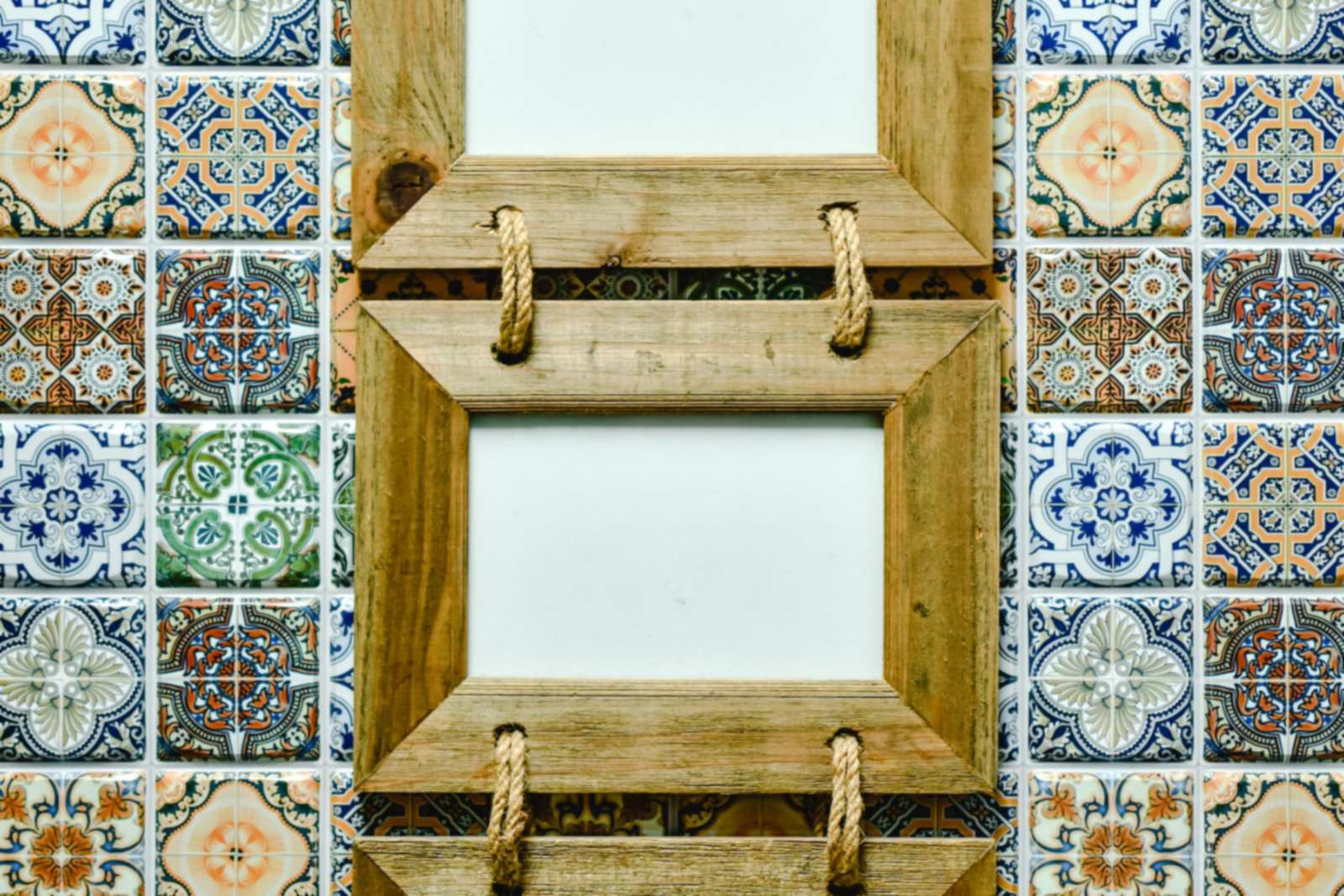 Rustic wooden frames suspended one below another from a rope against a colorful patterned tile wall, hung without individual nails.