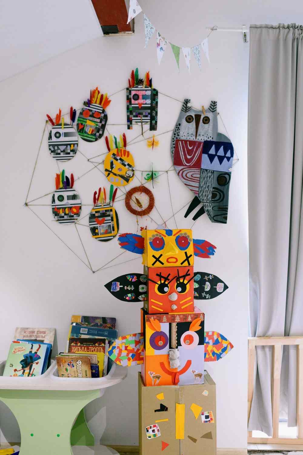 Children's room wall decorated with colorful flat paper crafts, including an owl, hung on strings