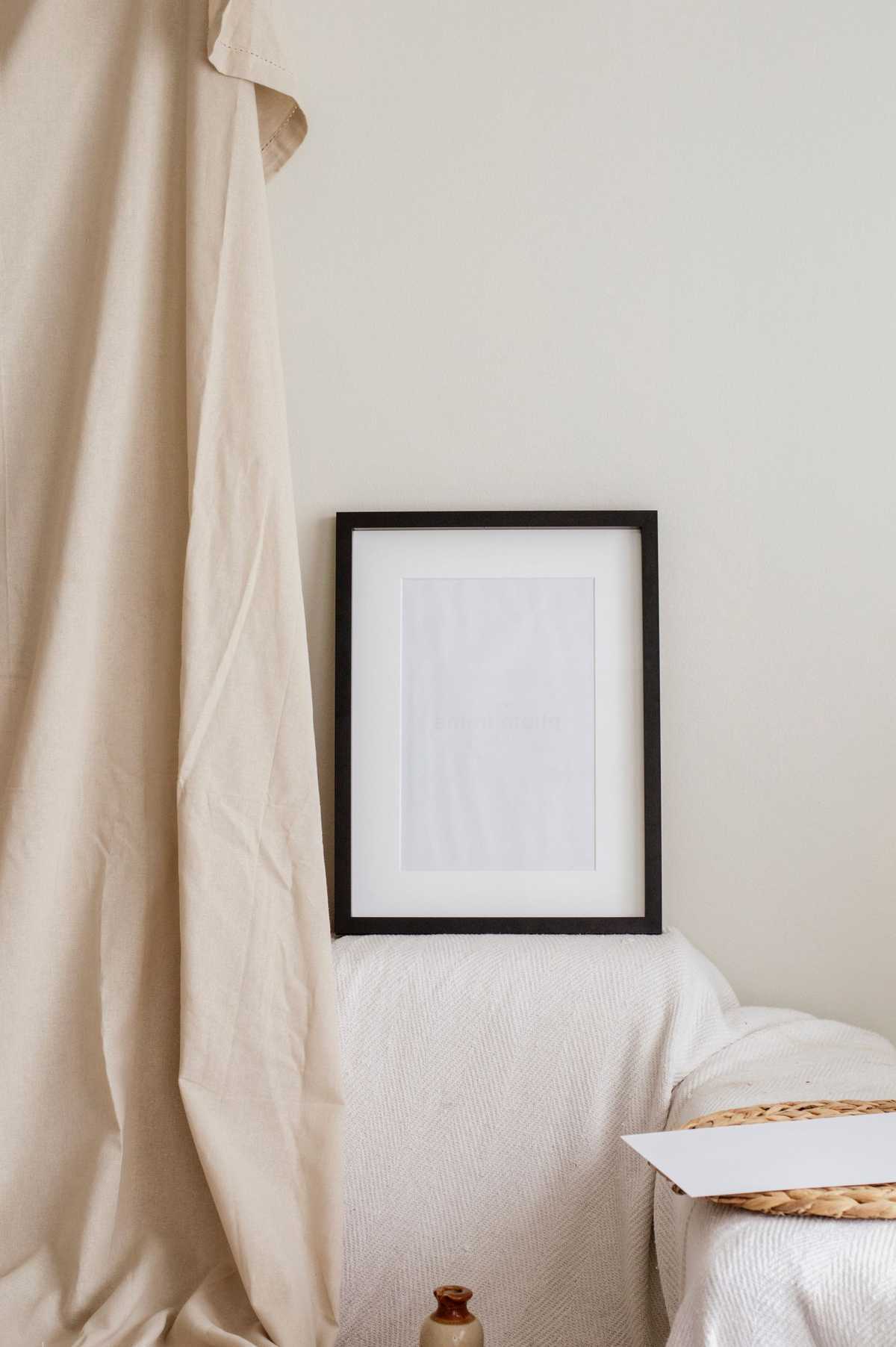 Black-framed picture leaning against a white wall beside draped fabric and a sofa