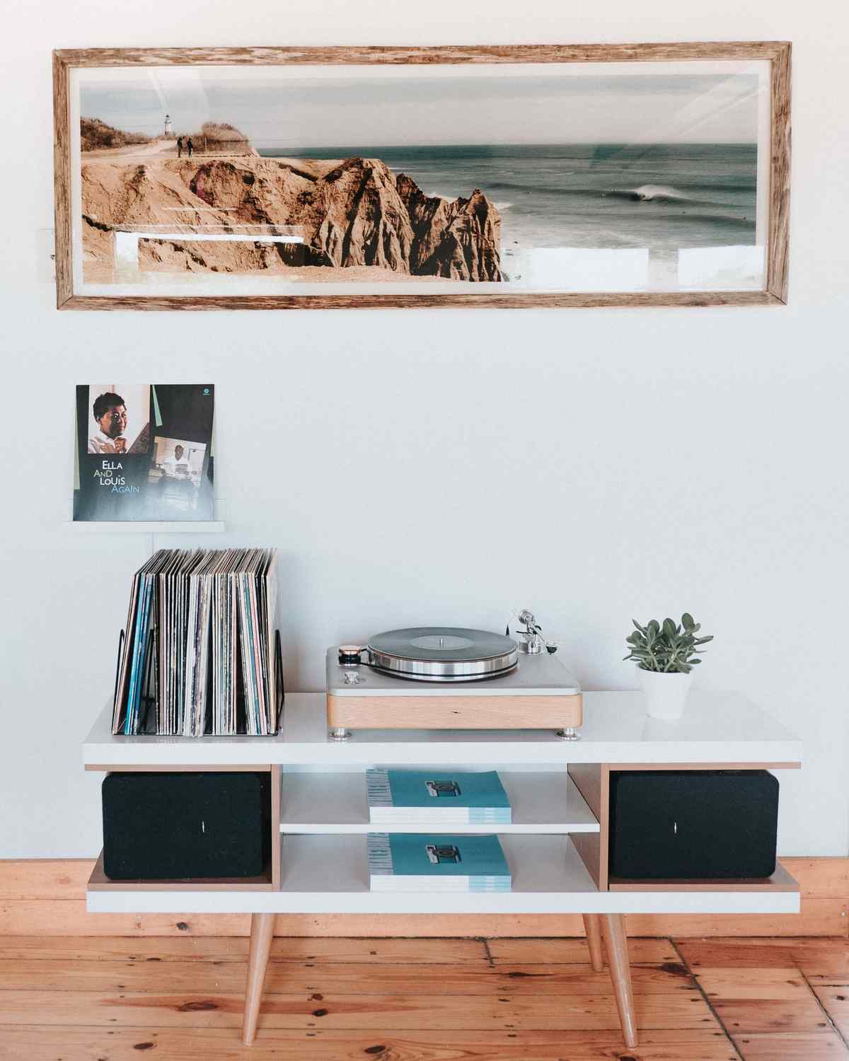 Listening corner with a record player and speakers on a low console, vinyl records, and a large framed coastal photograph on the wall above