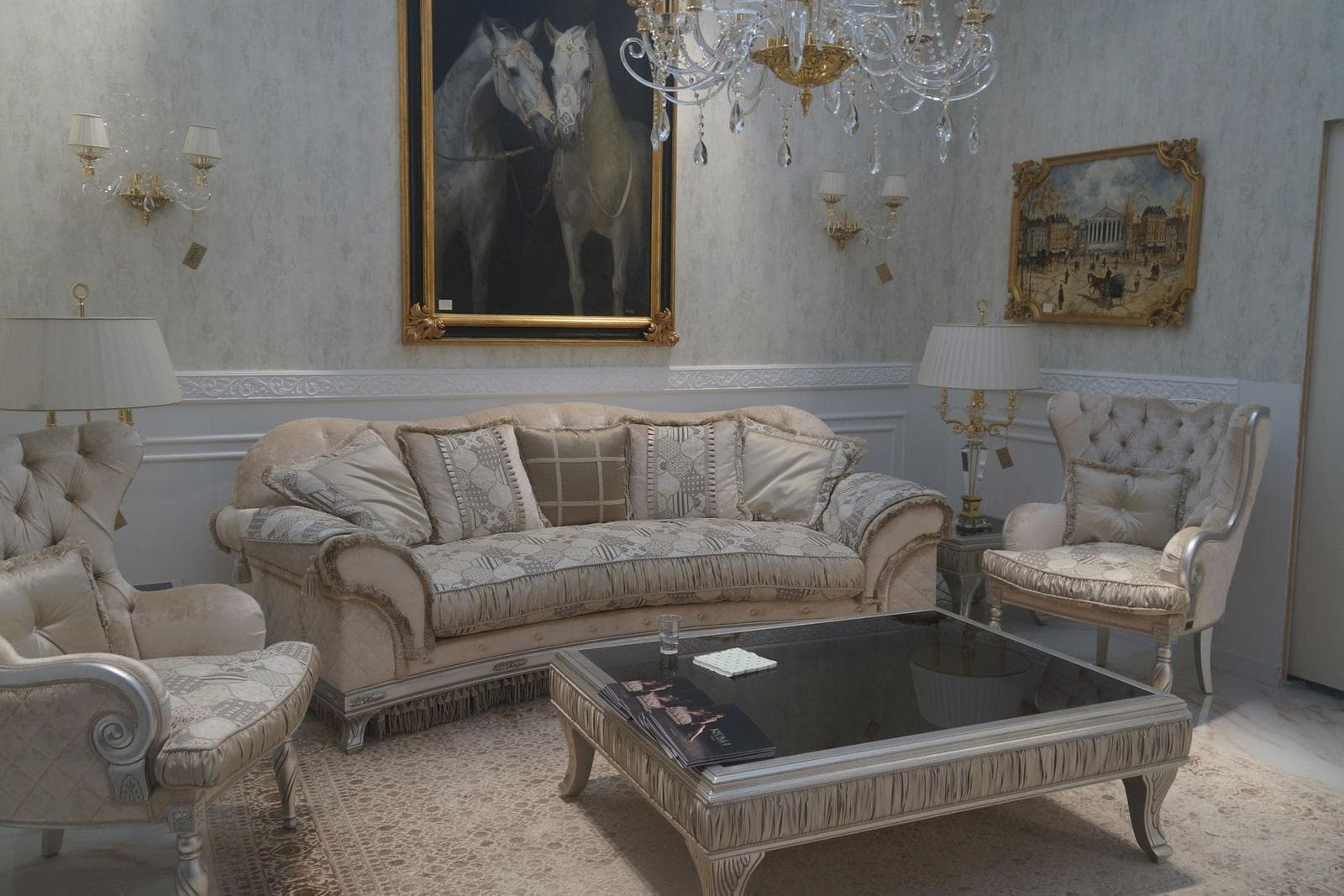Classic living room with a large gilt-framed painting of two horses above an ornate cream sofa, with a second framed artwork on the wall beside it.