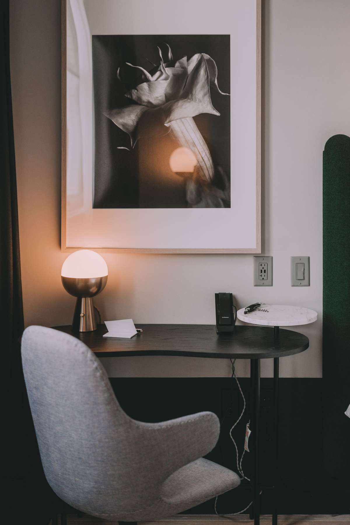 Large black-and-white floral photograph in a wide white mat and thin frame hanging above a desk and lamp