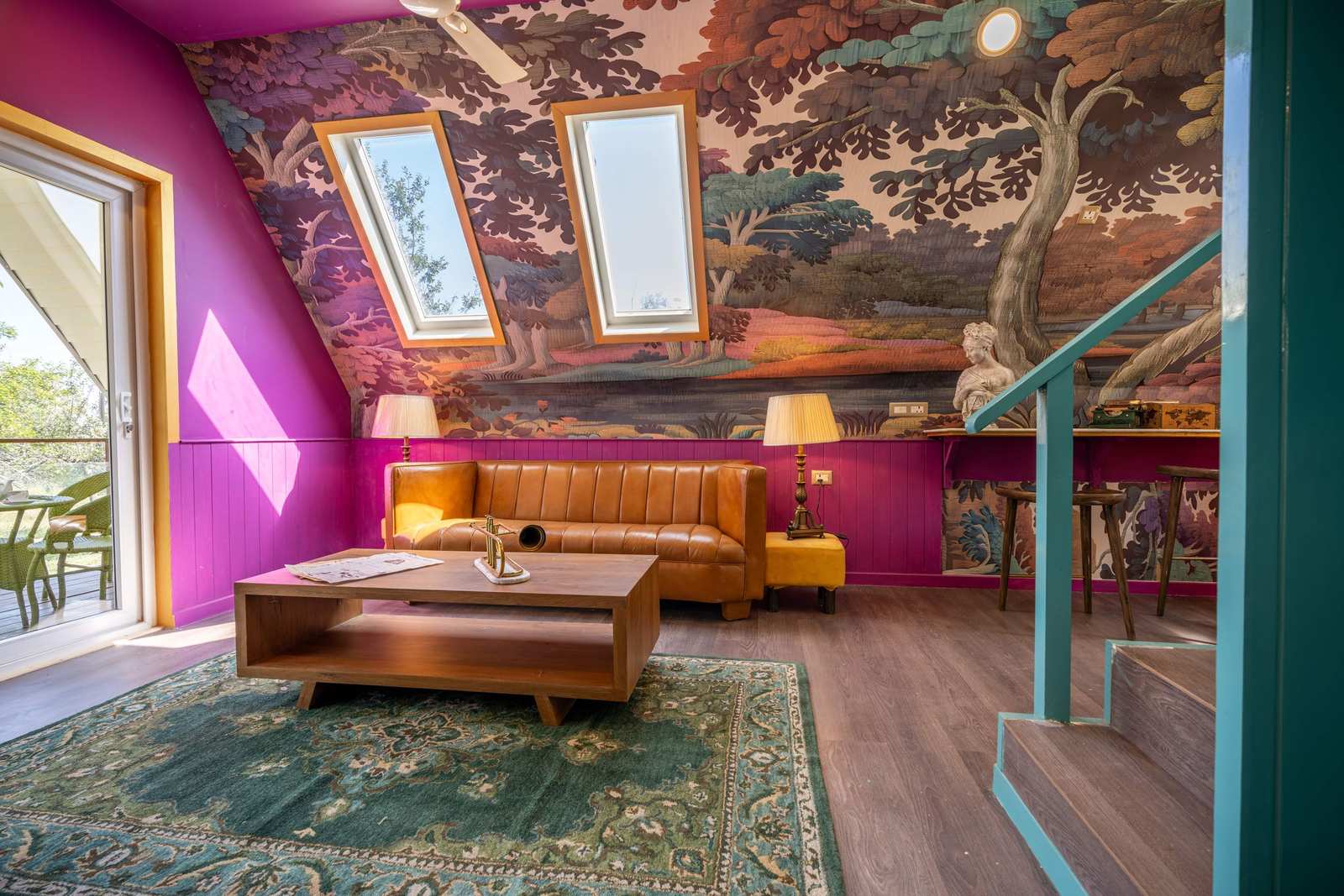 A maximalist attic living room with magenta walls, a scenic tree mural wallpaper, a tan leather sofa and a classical bust