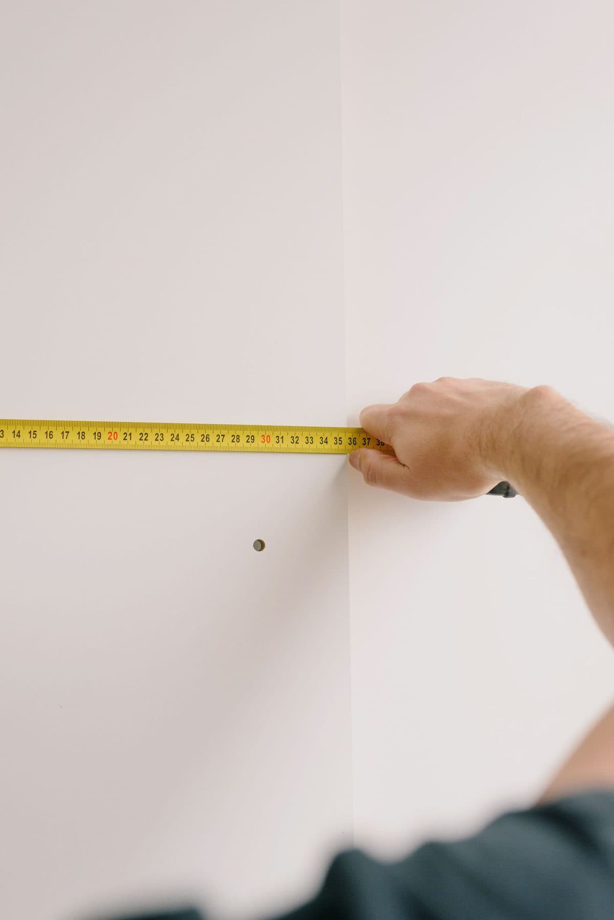 Hand holding a yellow tape measure against a white wall to measure its width