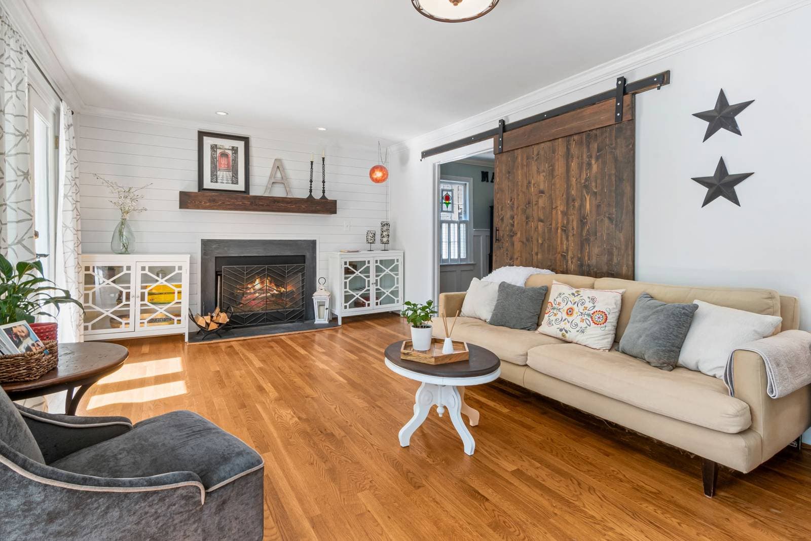 A modern farmhouse living room with white shiplap walls, a sliding barn door, a framed print above the fireplace mantel and black metal star wall decor