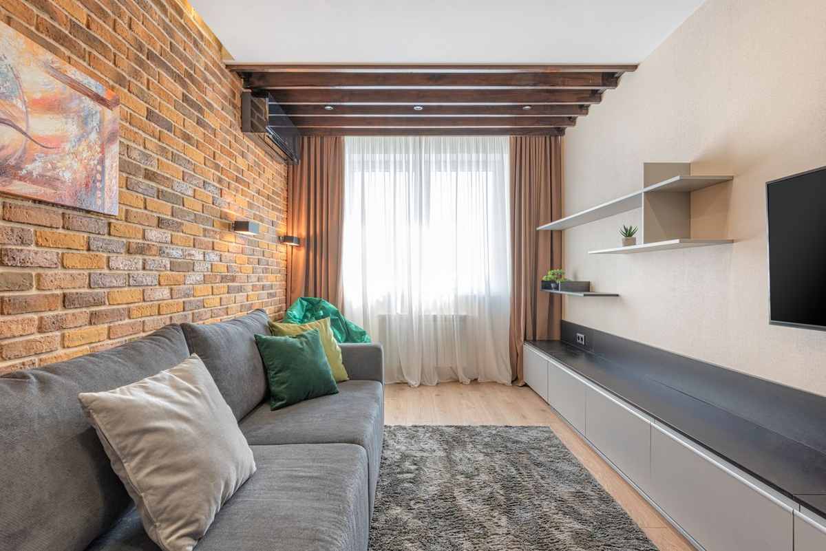A living room with an exposed brick wall and a canvas painting hanging on the brick above a grey sofa
