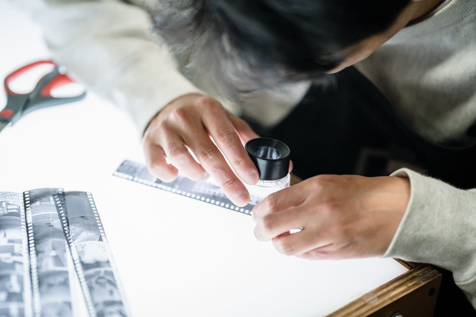 A person examining a strip of photographic film with a loupe on a light table.