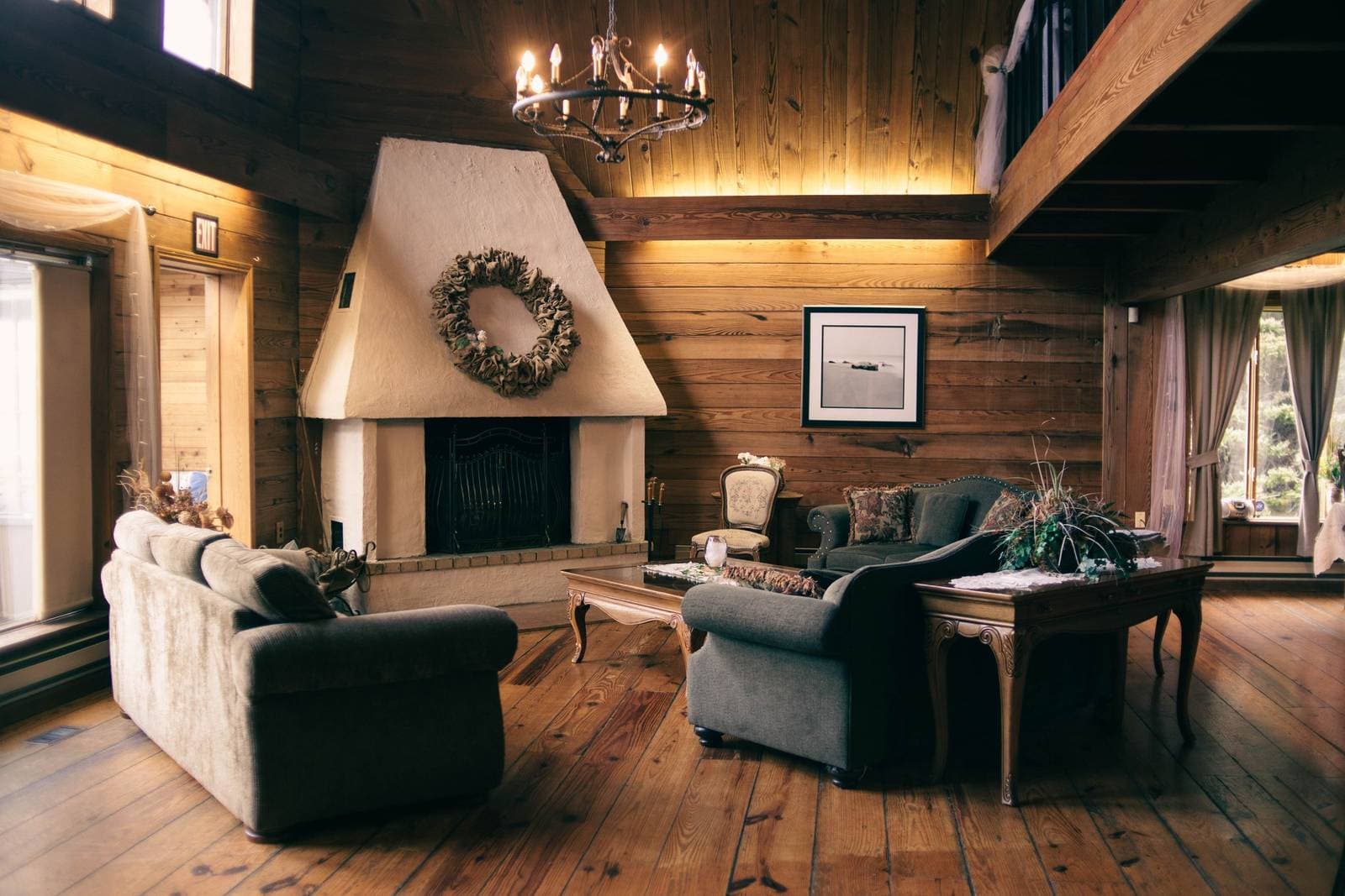 A wood-paneled cabin living room with a large fireplace, a wreath above the mantel and a framed black-and-white print on the timber wall
