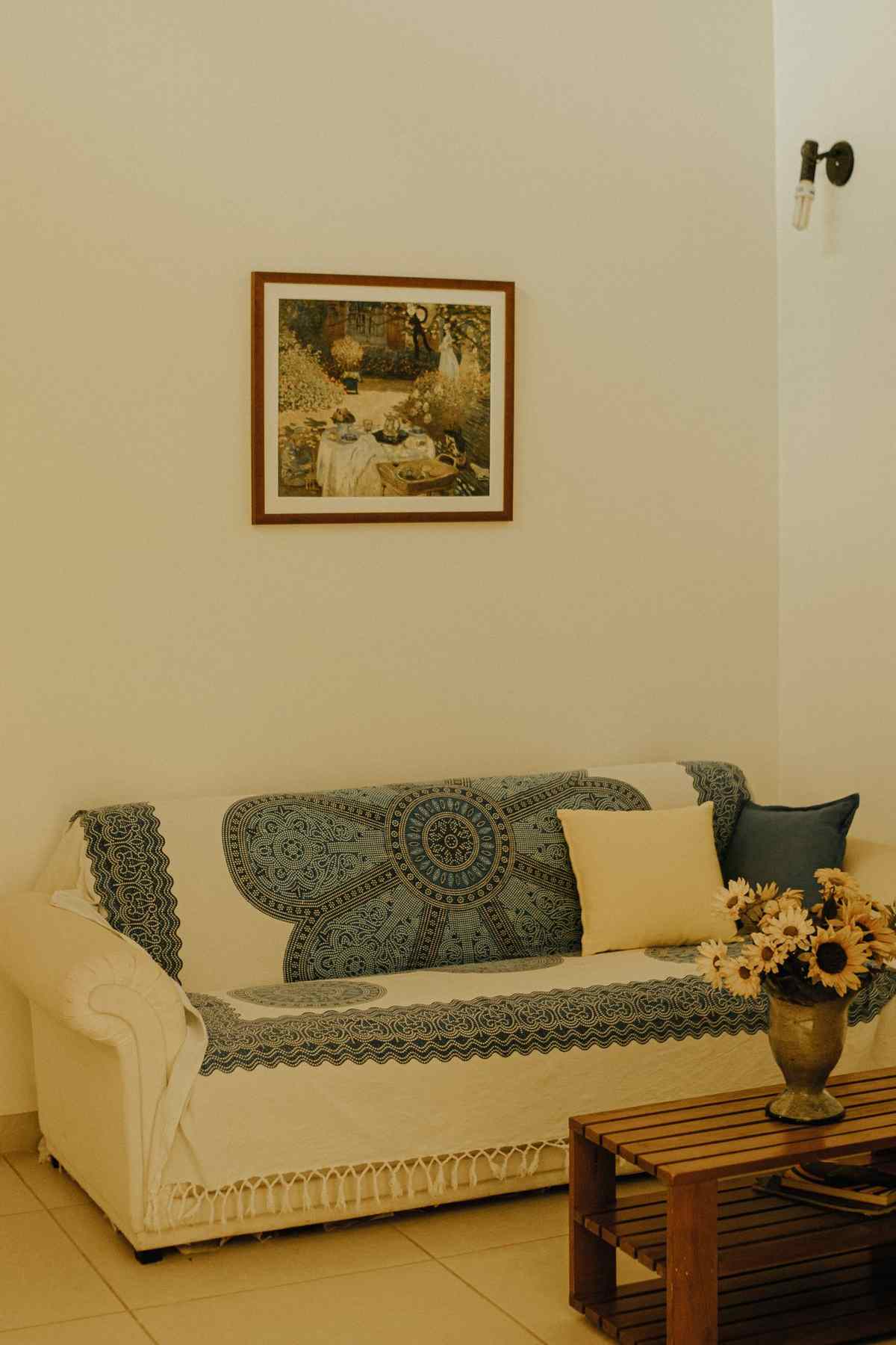 A simply furnished living room with a framed painting above a patterned sofa and a vase of sunflowers on the coffee table
