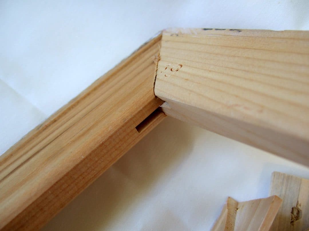 Close-up of a wooden canvas stretcher bar corner showing the tightening slot for a corner key