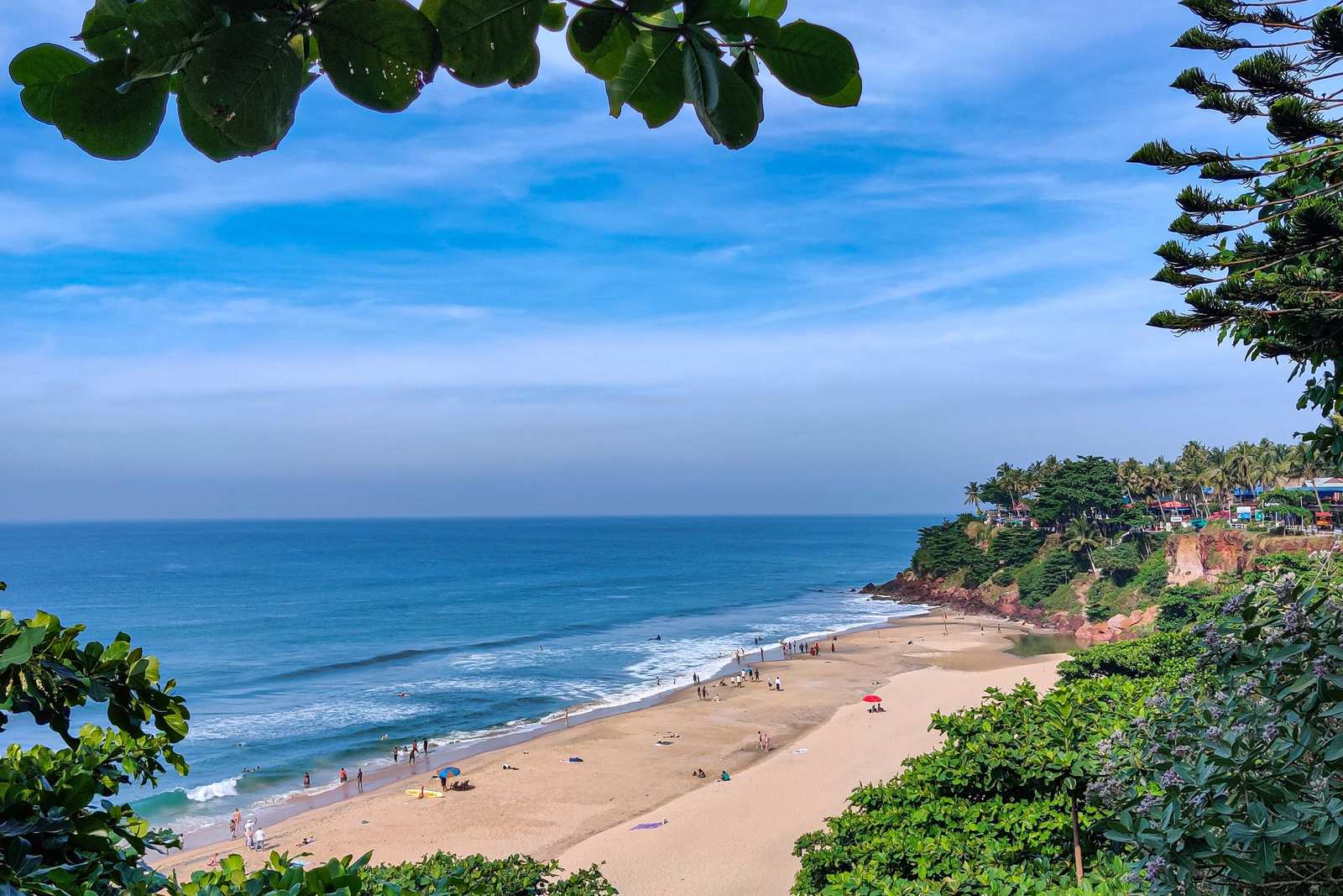 A sunny tropical beach with turquoise water and golden sand framed by lush green leaves.