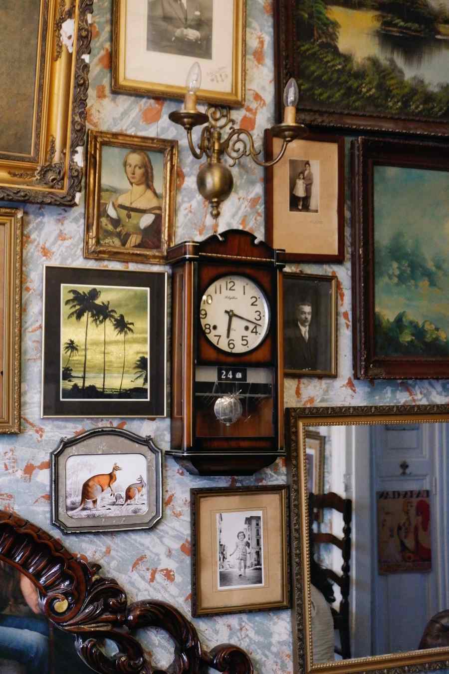 A densely filled vintage gallery wall of framed portraits, paintings and photographs around an antique wall clock